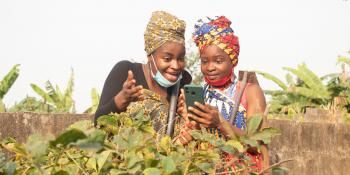 two ladies wearing african attire at their farmland, two ladies looking into their phone.